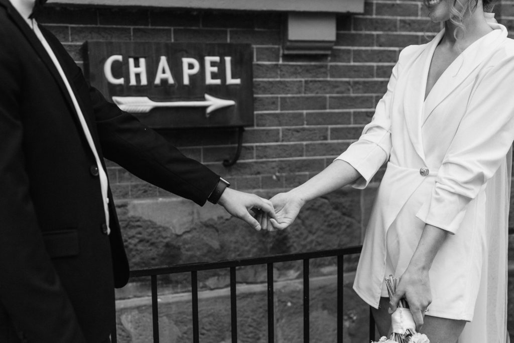 A black and white image of a couple holding hands in front of a Chapel sign.