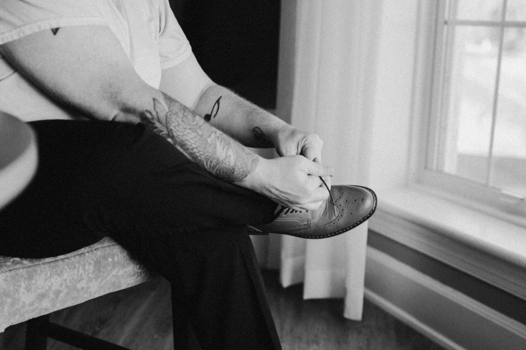 Black and white image of the groom tying his shoes on his wedding day.