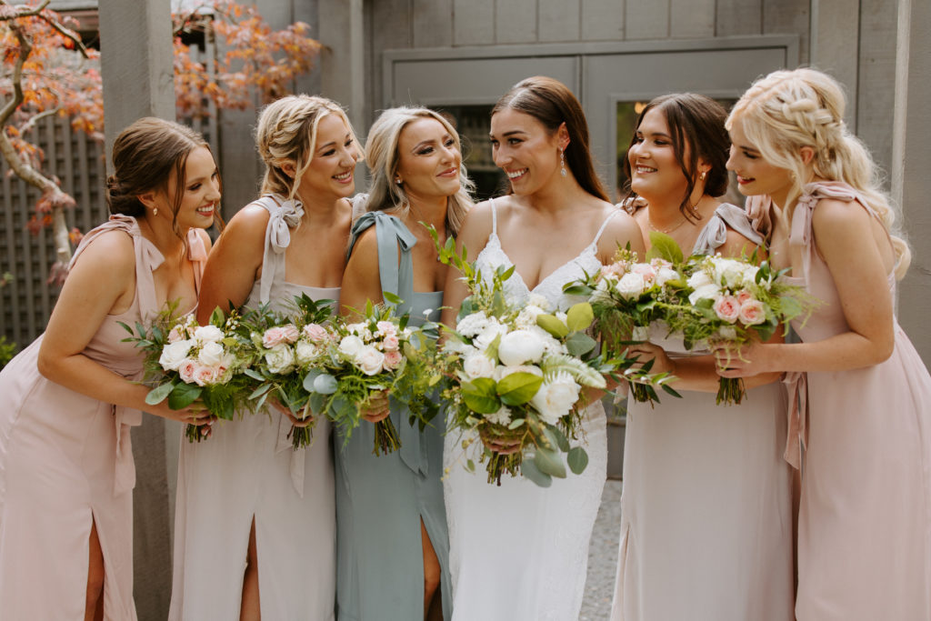 Bridesmaids are standing next to the bride and they are all laughing.
