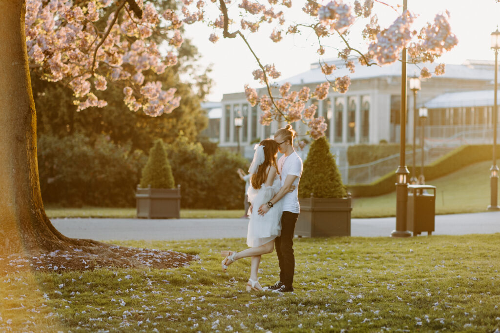 Couple posing under cherry blossom tree during golden hour