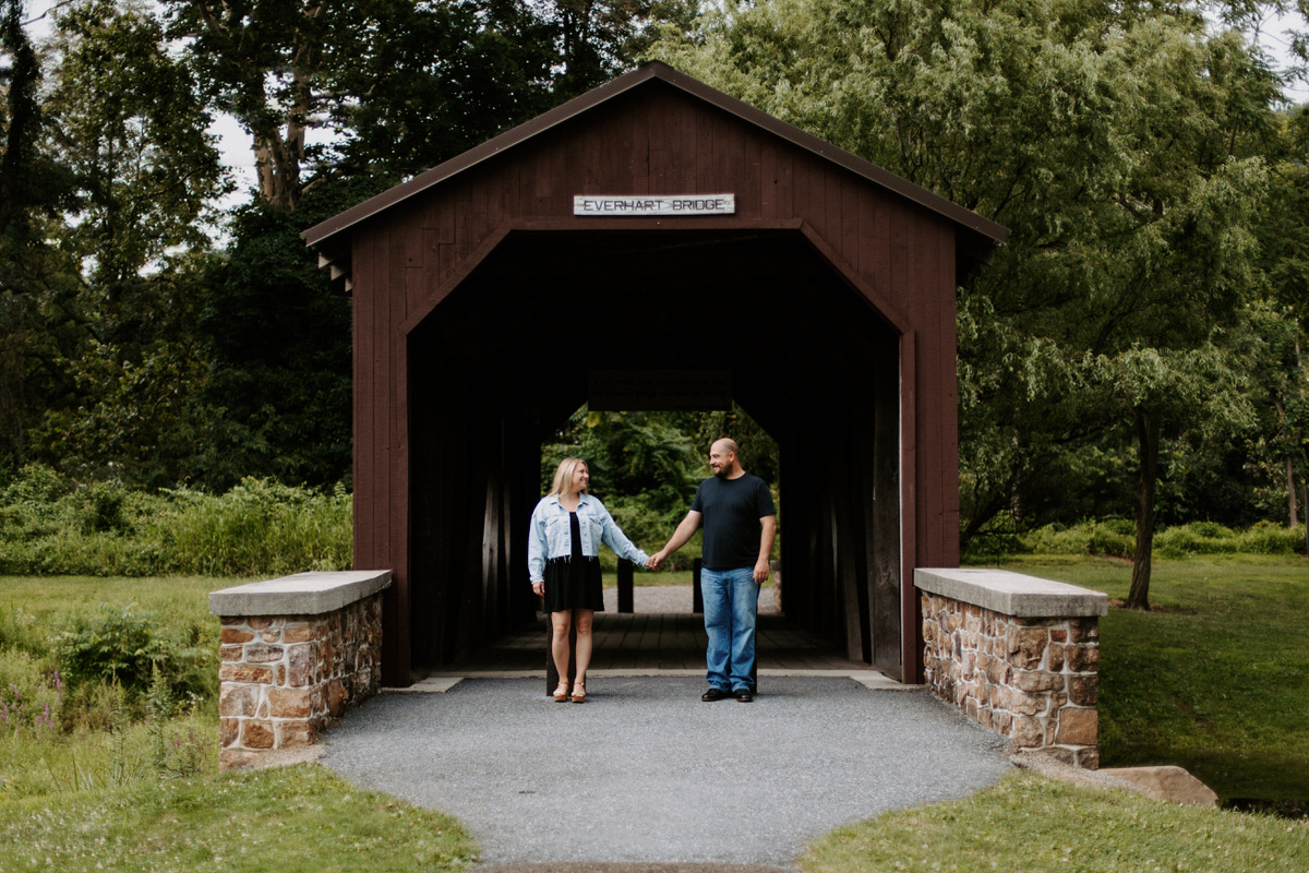 A couple holding hands and standing in front of a covered bridge at one of the best engagement session locations in Pennsylvania.