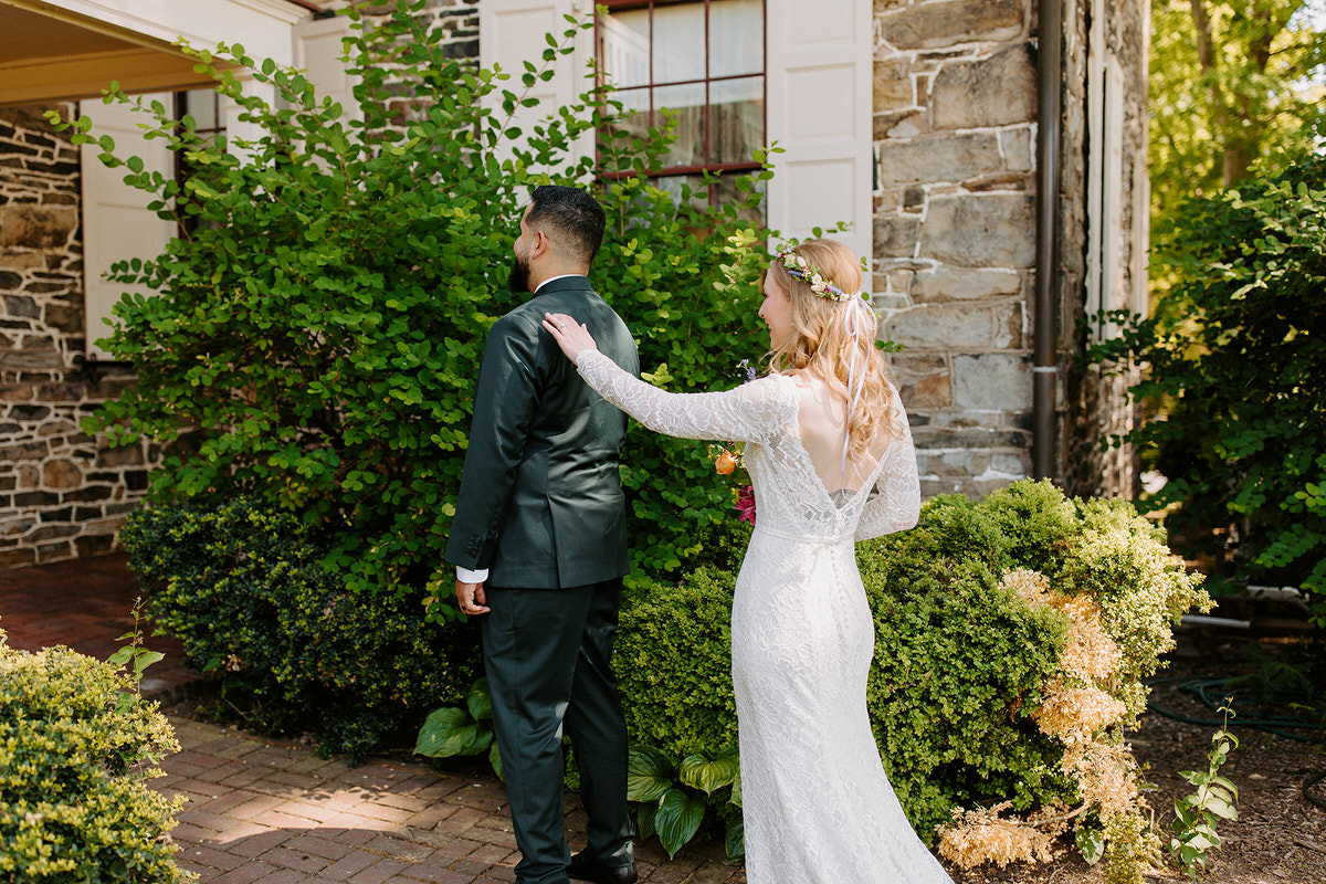 The pros and cons of doing a first look with a bride reaching out and touching a grooms shoulder while he faces the opposite way.
