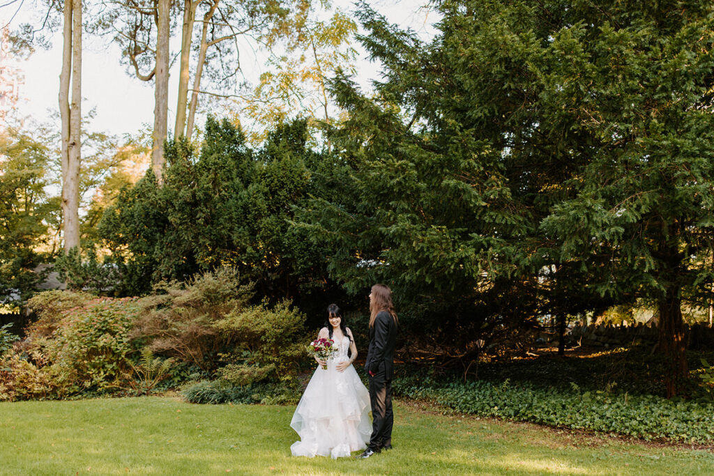 A bride and groom standing alone in a small wooded area during their first look. 