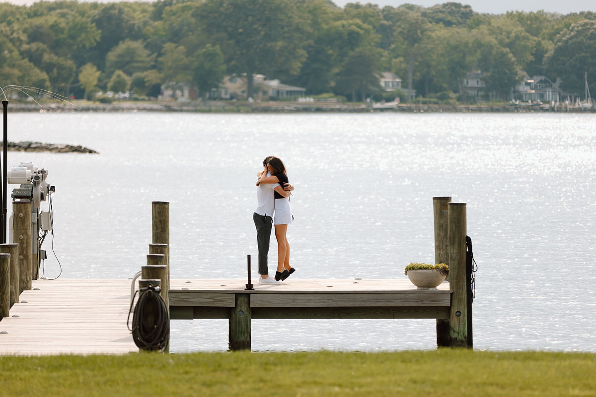 A couple hugging on a pier after getting engaged after one of them learned how to plan a secret proposal.