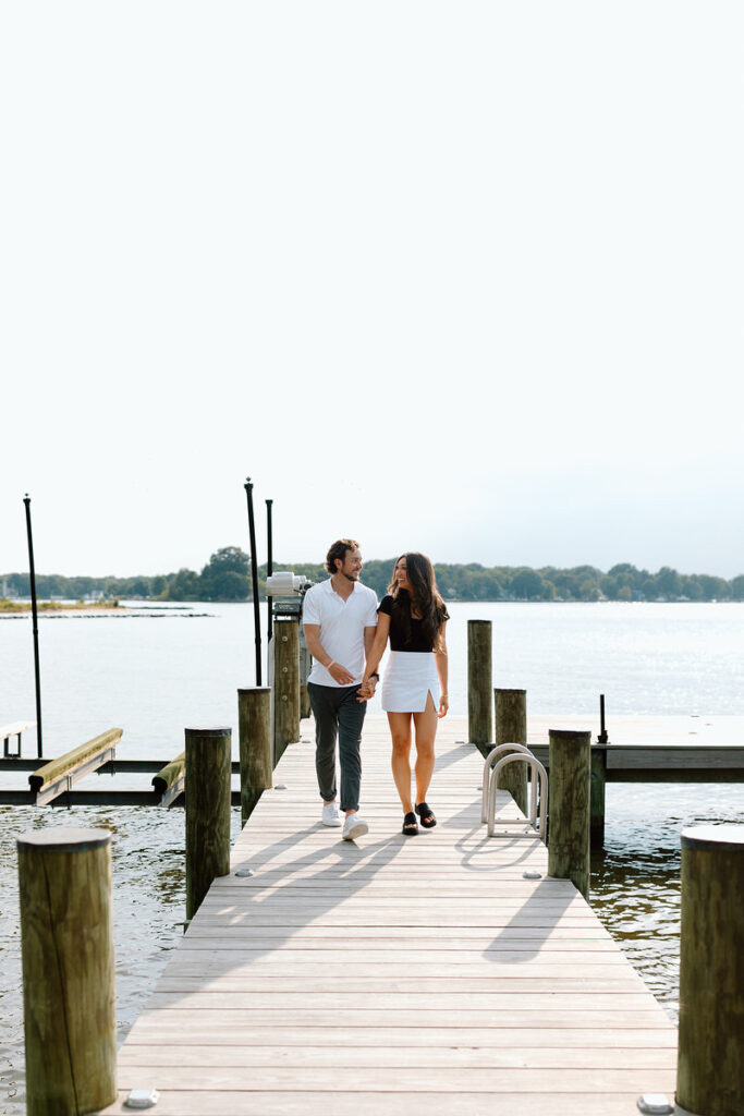 A couple holding hands and walking along a pier. 