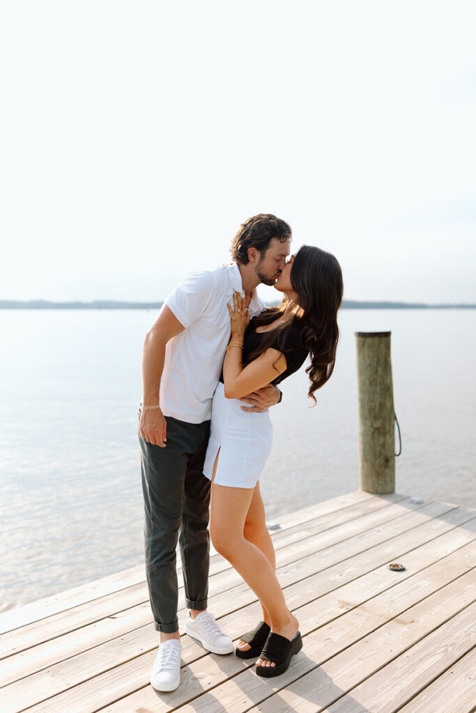 A couple kissing while standing on a pier. 