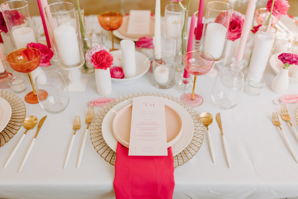 A detailed view of a place setting at a wedding reception with pink plates, napkins, cups, and flowers. 