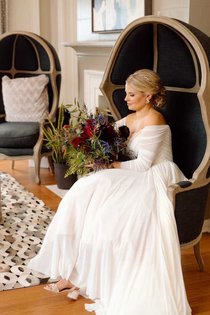 A bride sitting in an egg shaped, luxury chair holding a large bouquet of flowers. 