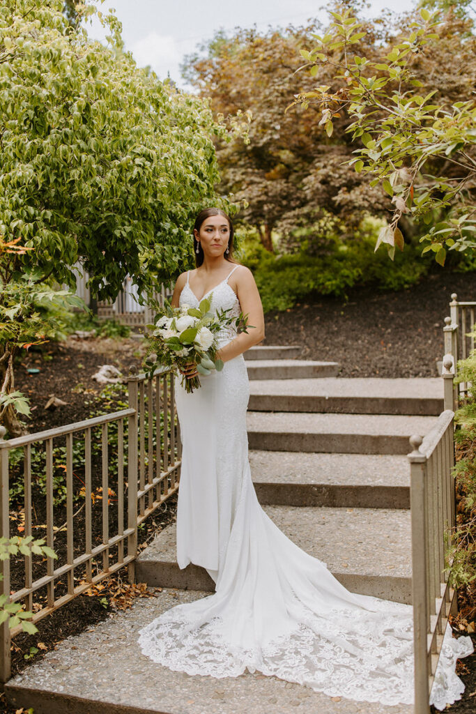 A bride standing on an outdoor, brick staircase holding her bouquet. 