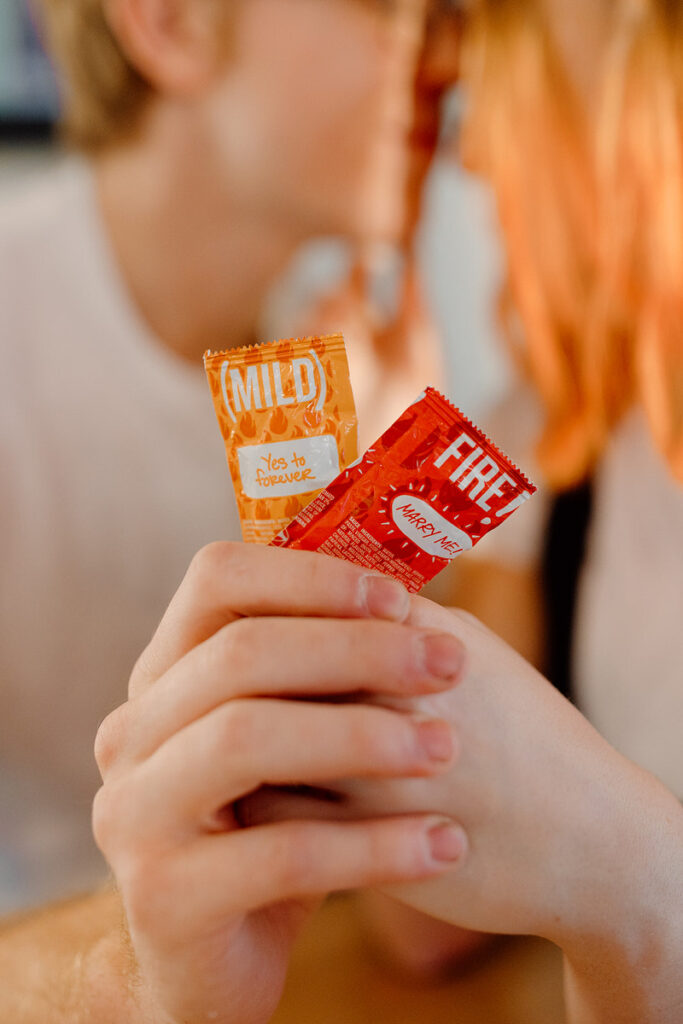 Two people holding hands while Taco Bell sauce packs are in them. 