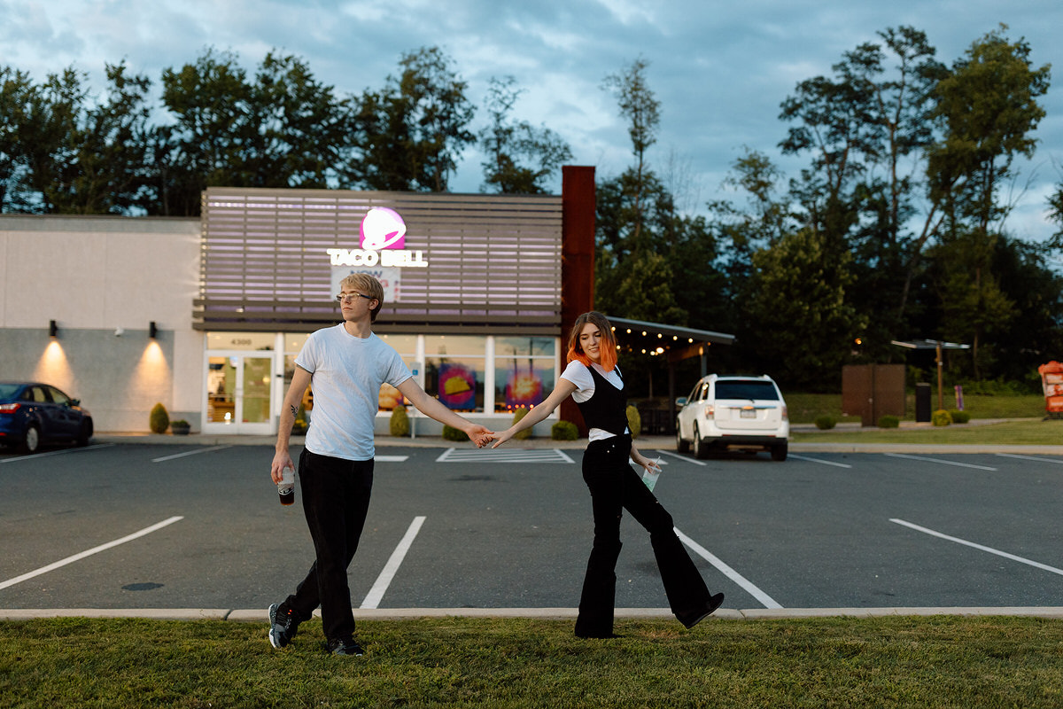 A couple holding hands and walking in parking lot in front of a Taco Bell during a Taco Bell photoshoot.