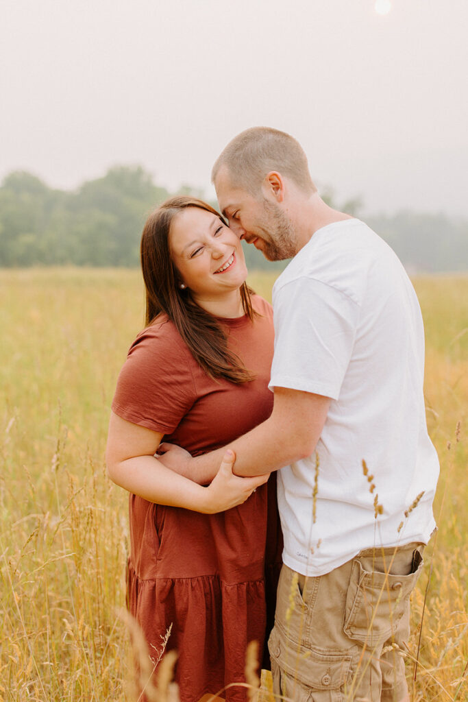 A man leaning down to kiss a woman's cheek as they stand in a field. 