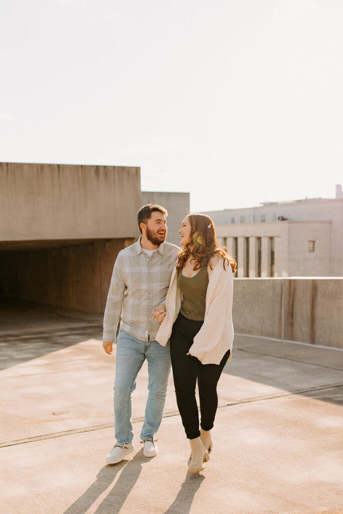A couple holding hands and walking along to top floor of a parking garage. 