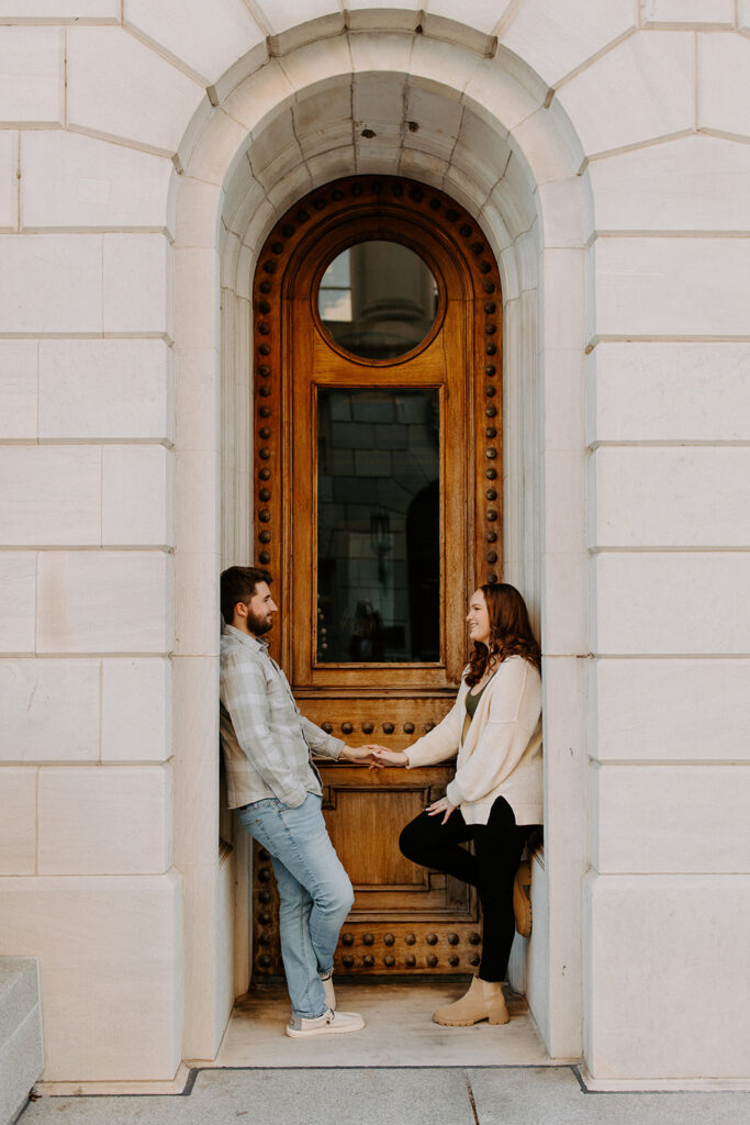 A couple reaching out to hold hands while they lean back on opposite sides of a small archway. 