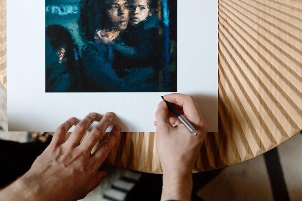 An artist holding a pen and signing the bottom of a piece of art. 