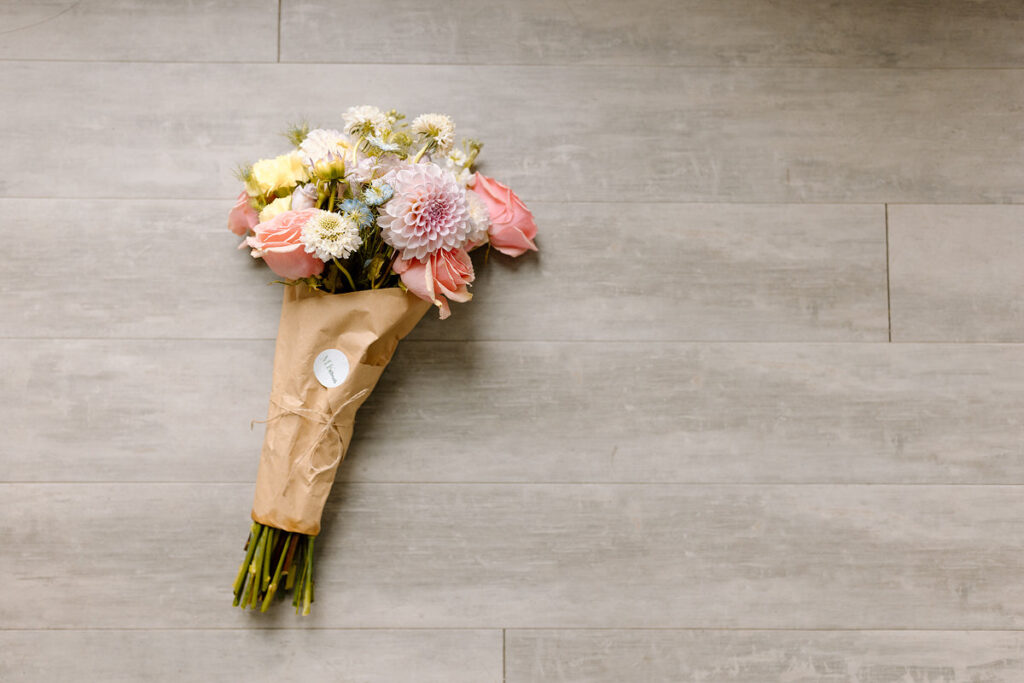 A floral arrangement wrapped in brown paper laying on the floor. 