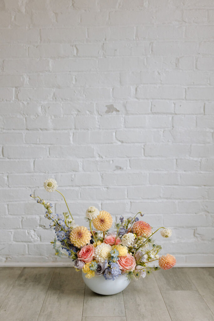 A flower arrangement in a pot sitting in front of a white brick wall. 