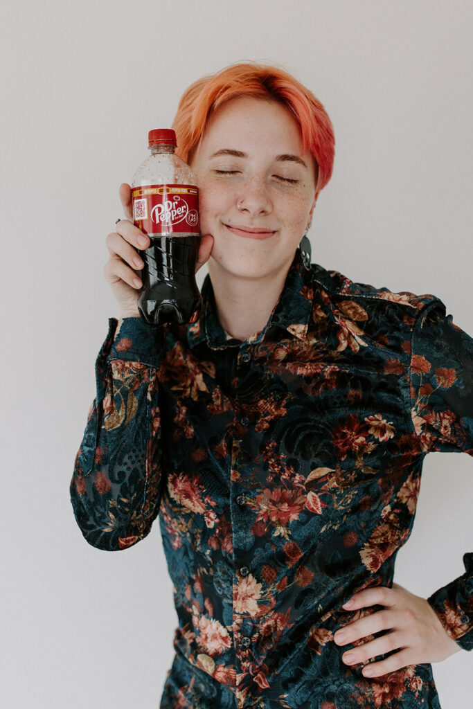 A person with their eyes closed as they hold a bottle of Dr. Pepper up to their face. 
