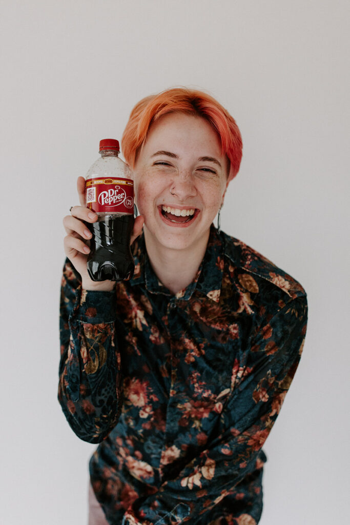 A person smiling and holding up a bottle of Dr. Pepper. 