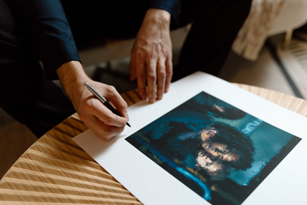 An artist signing the bottom of a print. 