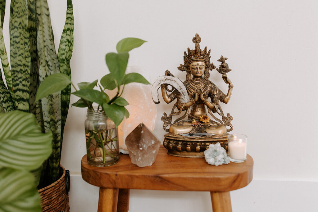 A wooden stool with gems, candles, a statue, and a small plant on it. 