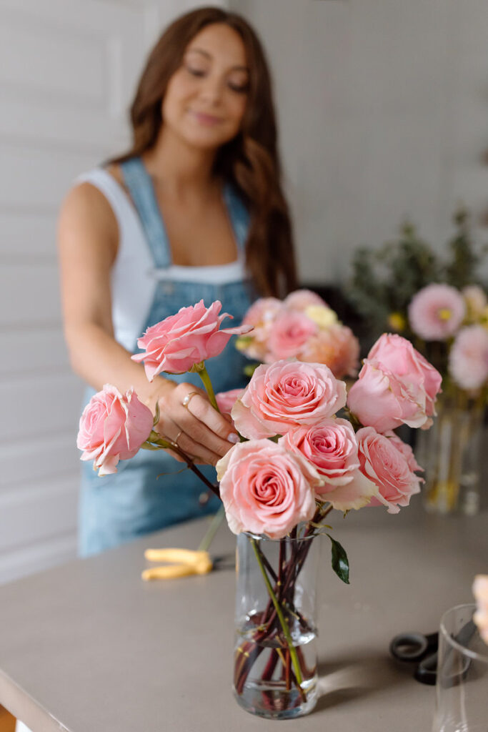 A vase of pink flowers with a florist standing behind it. 