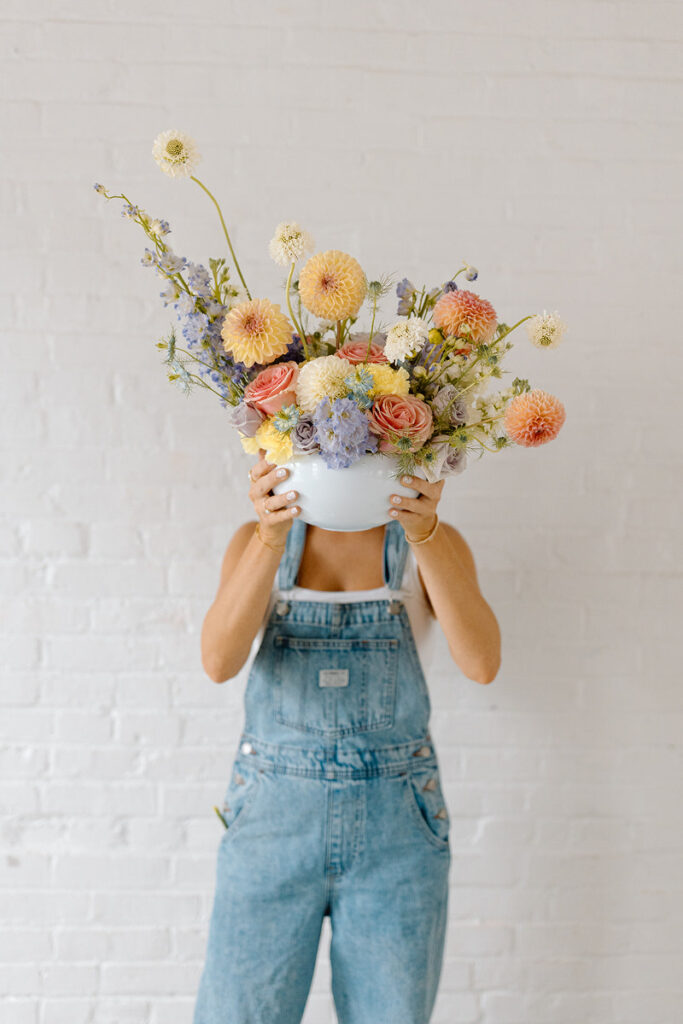 A person holding a large vase full of flowers over their face.