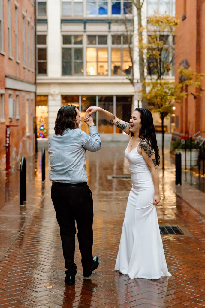 A playful and joyful dance in the rain, with one person twirling the other by the hand, both laughing and enjoying the moment on a wet cobblestone path.