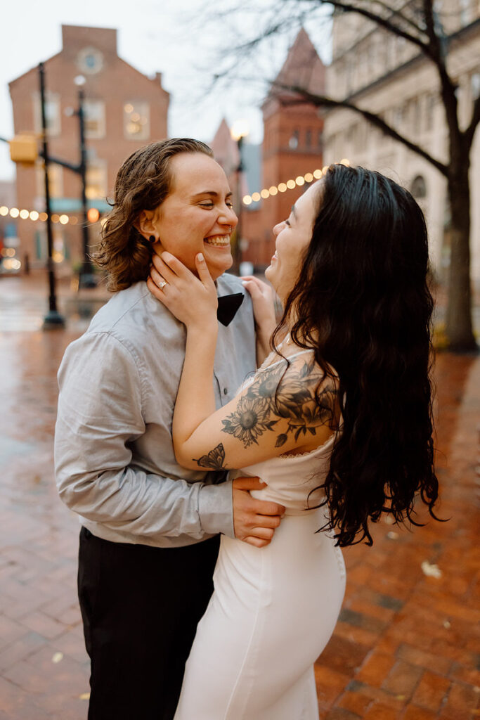 A close-up of the couple in a loving pose on a city street, with a soft focus on the warm lights and raindrops around them.