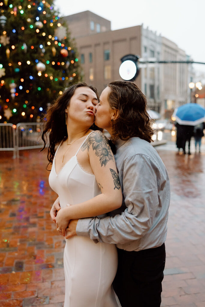 A close-up of the couple in a loving pose on a city street, with a soft focus on the warm lights and raindrops around them.