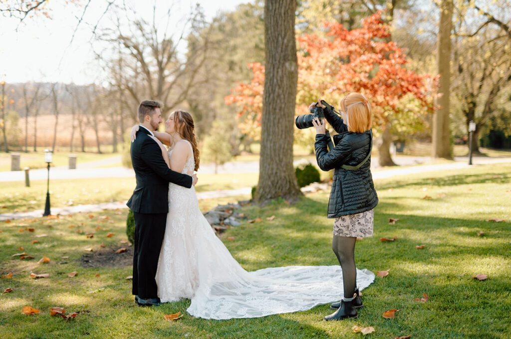 A photographer captures a loving moment between a bride and groom outdoors, with the couple standing close together and the bride holding a long, flowing gown.