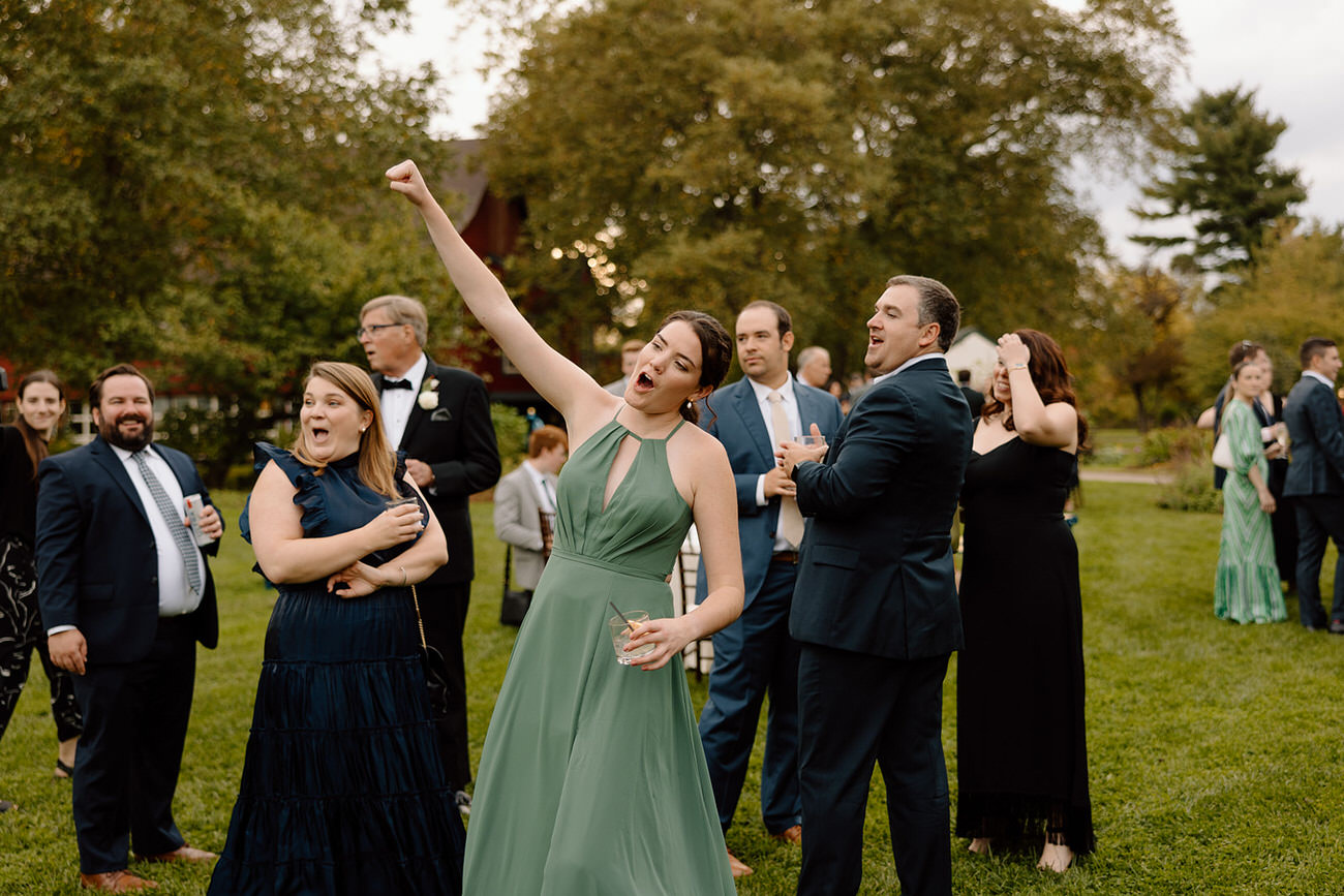 A joyous moment captured with a wedding guest in a green dress raising her arm triumphantly, surrounded by other celebrating guests.