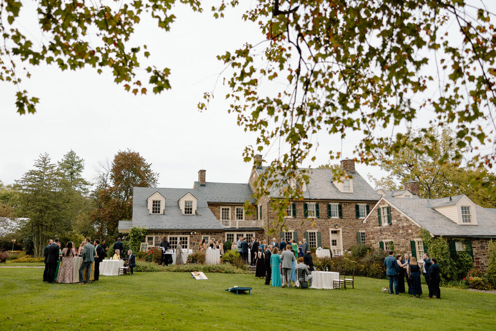 Guests mingling on the lawn of an elegant country house during a wedding reception, with the house providing a beautiful historic backdrop.