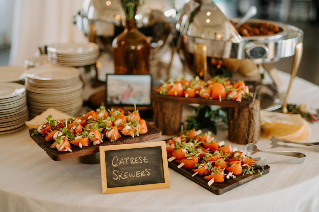 A well-presented buffet table with a selection of Caprese skewers on wooden trays and a small blackboard sign, ready for guests at a wedding reception.