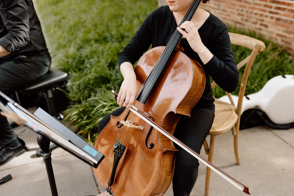 A cellist in black attire playing a classical piece on a cello, part of a live music ensemble for a sophisticated wedding ambiance.