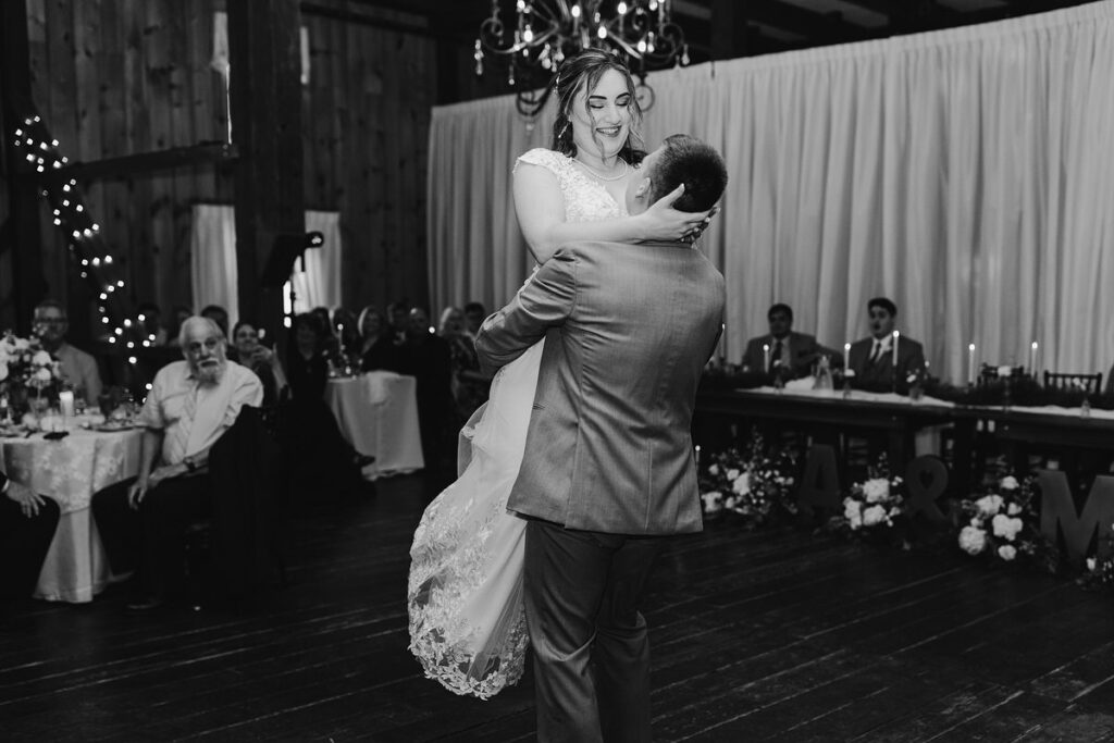 The bride and groom share a first dance under a rustic wooden ceiling, illuminated by twinkling lights