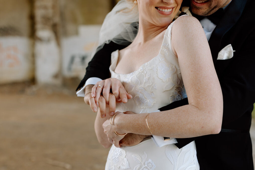 A newlywed couple hugging from behind. 