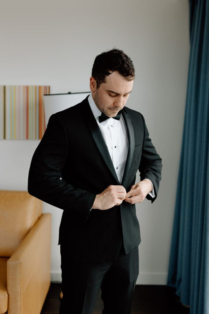 A person buttoning their suit jacket as they get ready for their wedding. 