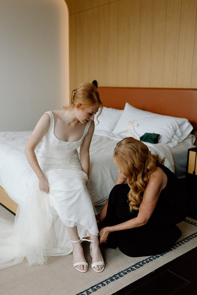 A person helping a soon to be wed put on their shoes before their wedding. 
