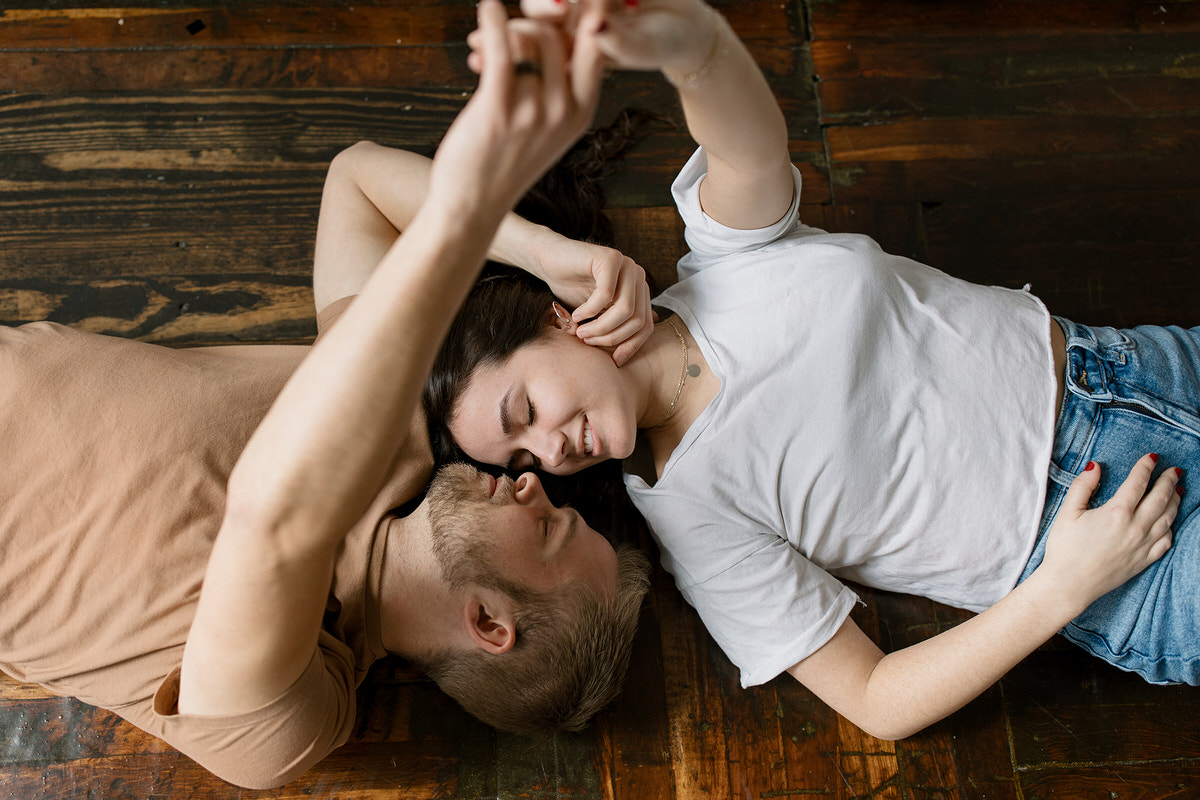 Overhead view of a couple lying on a hardwood floor, smiling and holding hands, creating a relaxed and intimate atmosphere