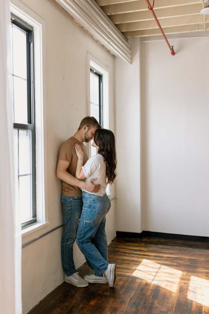 "A couple in a warm embrace by the window, sun casting a glow on their casual attire, sharing a private moment