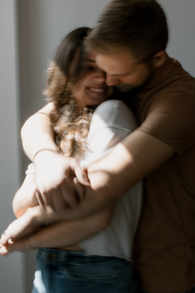 A blurred image of a couple embracing in a sunlit room, capturing an intimate and candid moment.