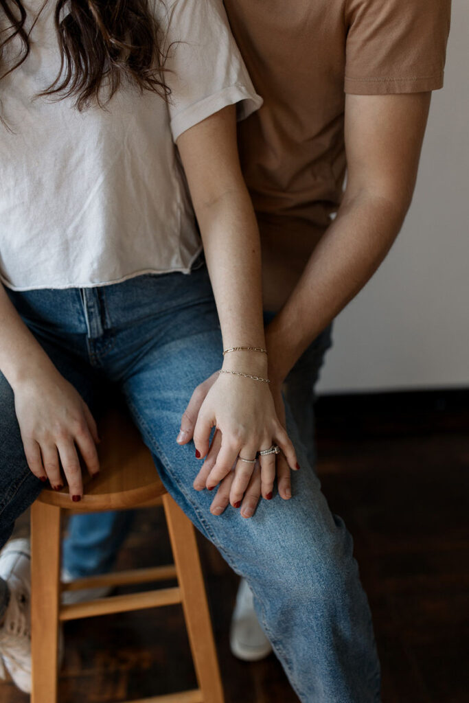 Close-up of a couple's hands entwined, showcasing engagement rings and casual attire, conveying a sense of connection
