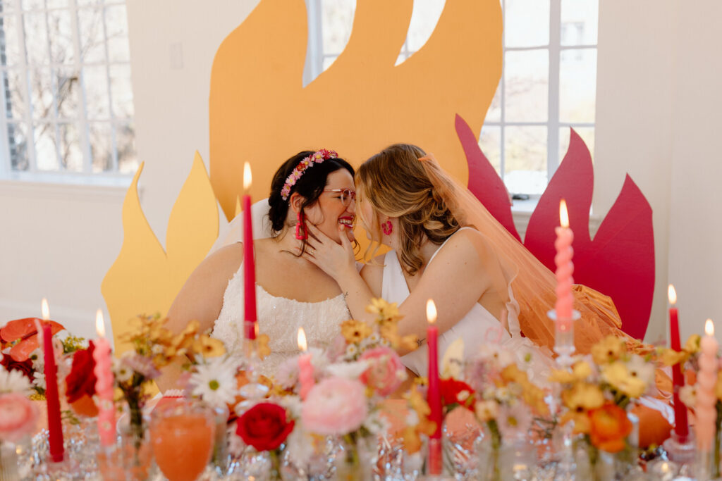 A couple goes in for a kiss at a wedding table surrounded by colorful flame decor and candles.