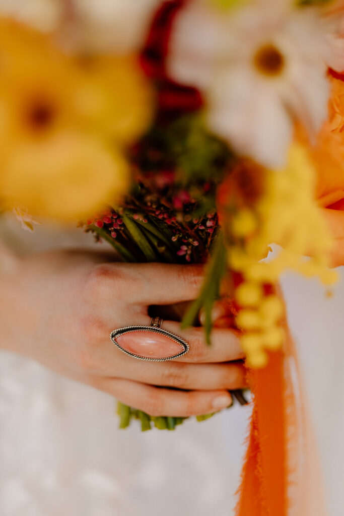 Close up of a hand with a ring holding flowers.