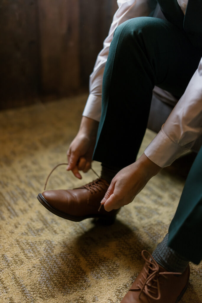 A to-be-wed sits in a chair tying their shoe.