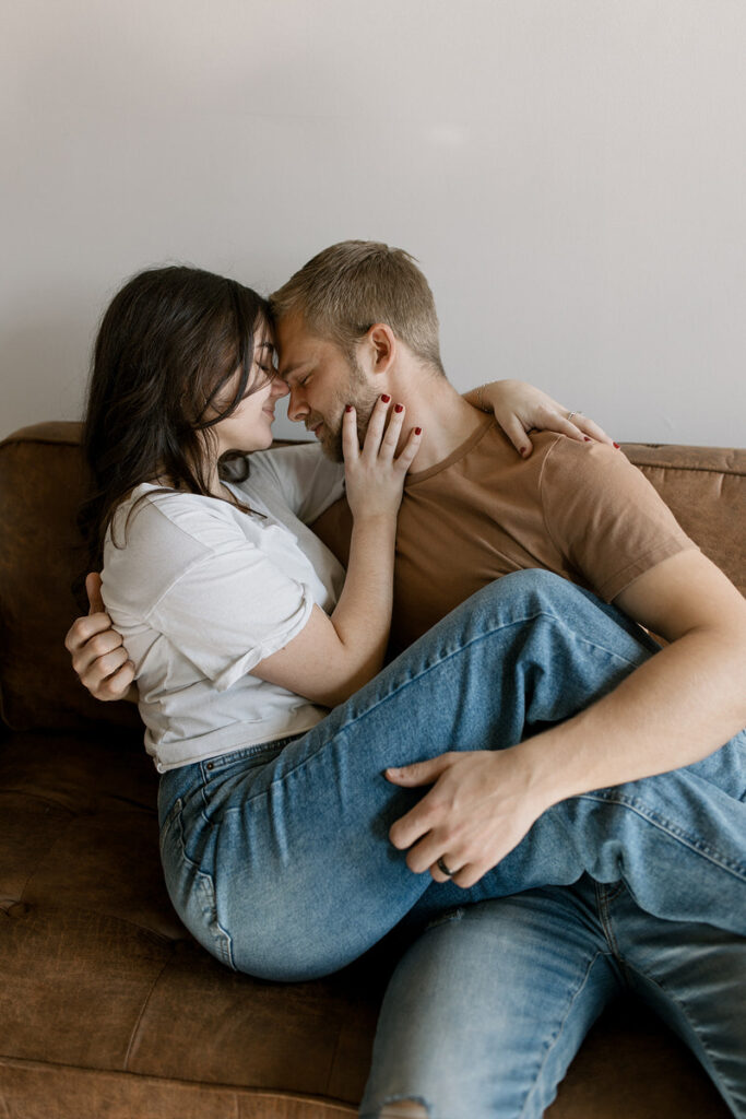 Two people with their foreheads together as they sit closely together on a couch 
