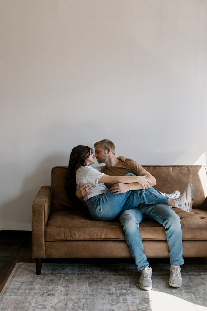 A person sitting on a couch with their legs over their partner next to them as they are about to kiss
