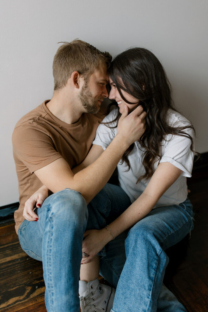 A couple sitting on the floor together intertwined with their foreheads touching 
