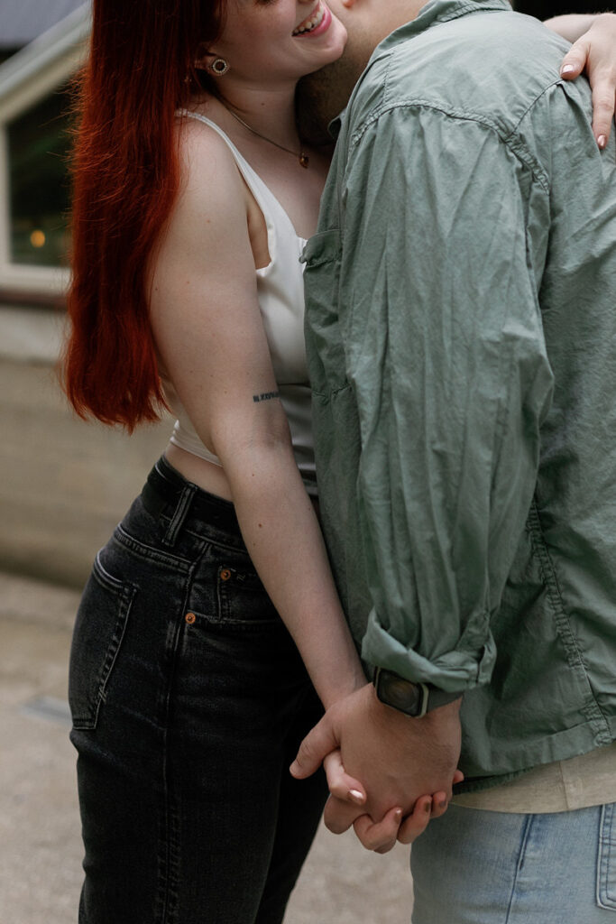 A close up of a couple holding hands while one kisses the other's neck 